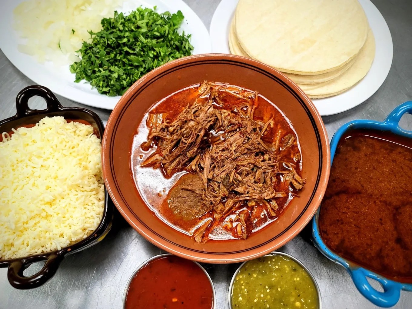 Birria with consomé, melted cheese, tortillas and fresh salsas