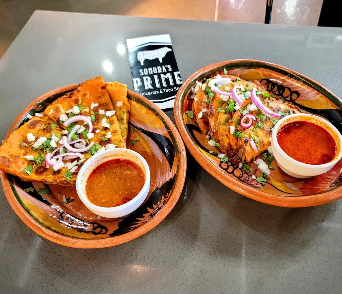 Two plates of quesabirria tacos and quesadilla with consomé